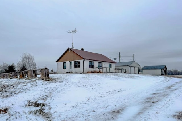 snow covered house with a detached garage and an outdoor structure