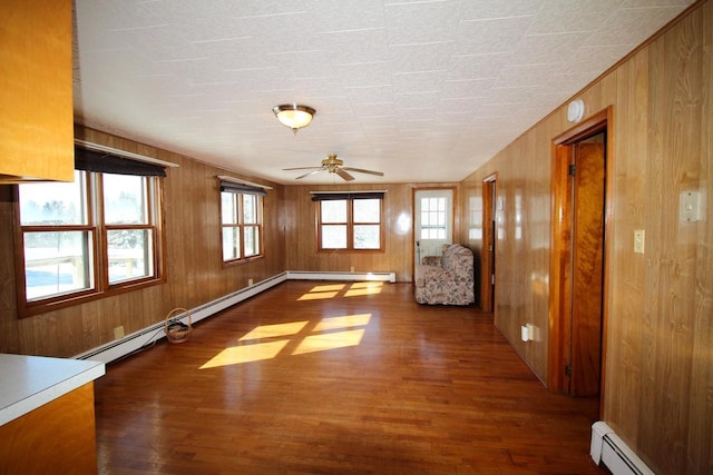 interior space with wood walls, baseboard heating, wood finished floors, and a ceiling fan