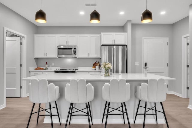 kitchen with light wood-type flooring, appliances with stainless steel finishes, white cabinets, and a large island with sink