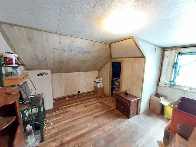 bonus room featuring lofted ceiling, light wood finished floors, and wooden walls