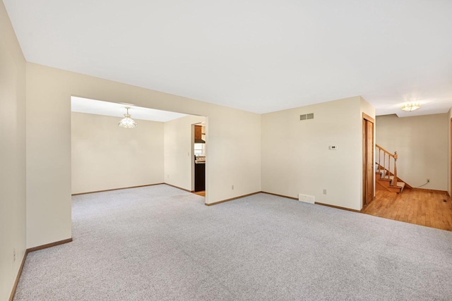 spare room featuring visible vents, carpet floors, a chandelier, and stairway