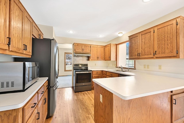 kitchen with a sink, under cabinet range hood, appliances with stainless steel finishes, a peninsula, and light countertops