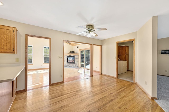 interior space featuring light wood-style flooring, washing machine and dryer, a fireplace, baseboards, and ceiling fan