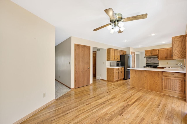 kitchen with under cabinet range hood, light wood-type flooring, appliances with stainless steel finishes, and a sink