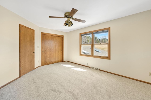 unfurnished bedroom with visible vents, two closets, ceiling fan, baseboards, and carpet