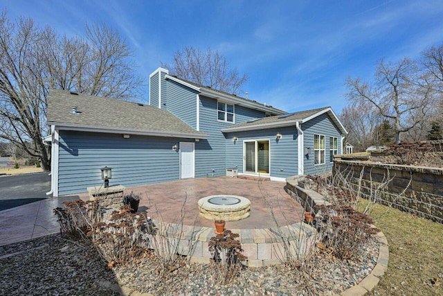 back of house featuring a patio area, a chimney, roof with shingles, and a fire pit