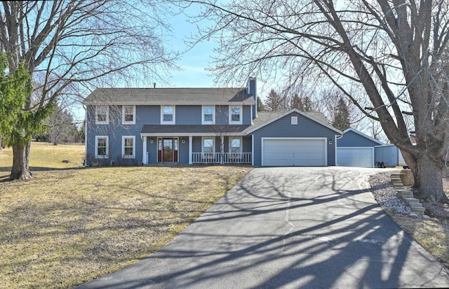 colonial-style house featuring aphalt driveway, a porch, an attached garage, a front yard, and a chimney