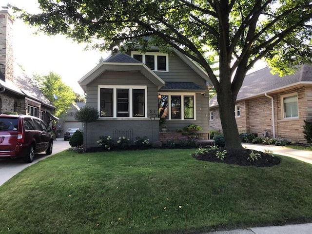 bungalow with a front lawn, brick siding, and a shingled roof