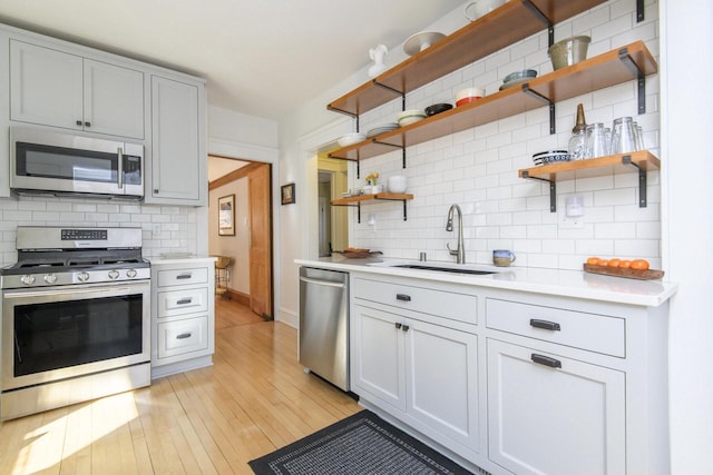 kitchen featuring a sink, light countertops, light wood-style flooring, stainless steel appliances, and open shelves