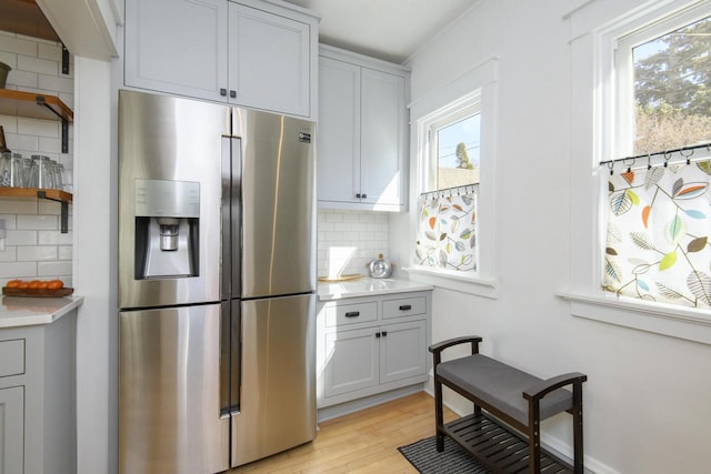 kitchen featuring decorative backsplash, light countertops, stainless steel refrigerator with ice dispenser, and light wood-type flooring