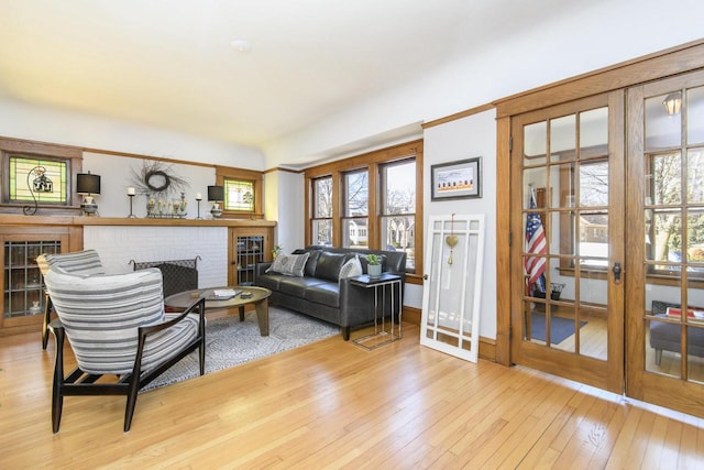 living room with a brick fireplace, baseboards, french doors, and light wood-style floors