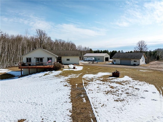 yard covered in snow with a detached garage, an outbuilding, and a wooden deck