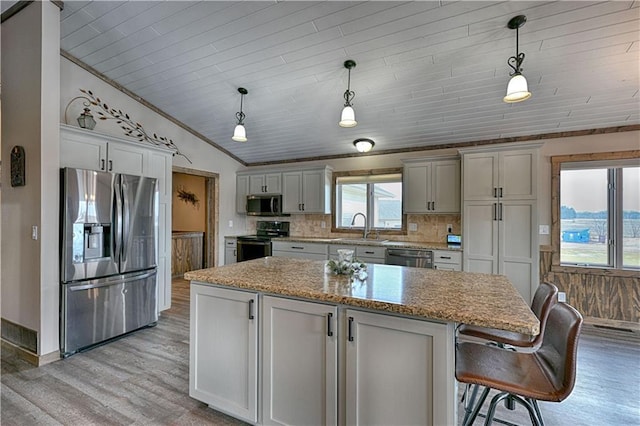 kitchen with lofted ceiling, a sink, appliances with stainless steel finishes, light wood-type flooring, and backsplash