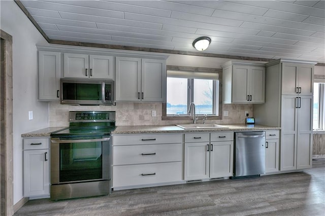 kitchen featuring light wood-style flooring, stainless steel appliances, a sink, backsplash, and light stone countertops