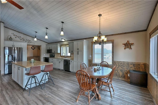 dining space with lofted ceiling, a wainscoted wall, a notable chandelier, and wood finished floors