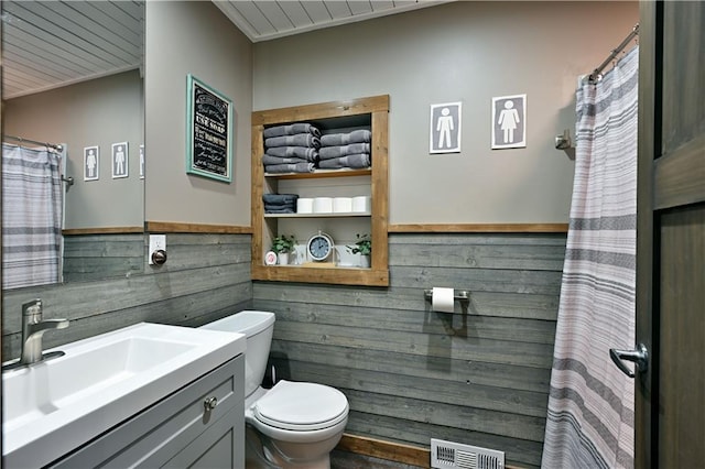 bathroom featuring toilet, wood walls, vanity, visible vents, and wainscoting