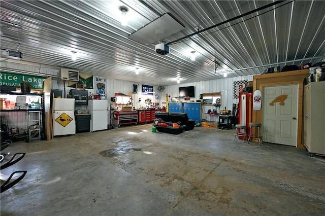 garage with a workshop area, metal wall, freestanding refrigerator, and a garage door opener