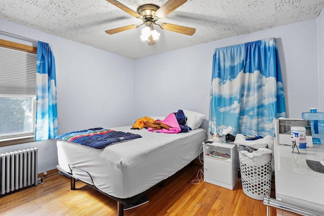 bedroom featuring a ceiling fan, radiator heating unit, and wood finished floors