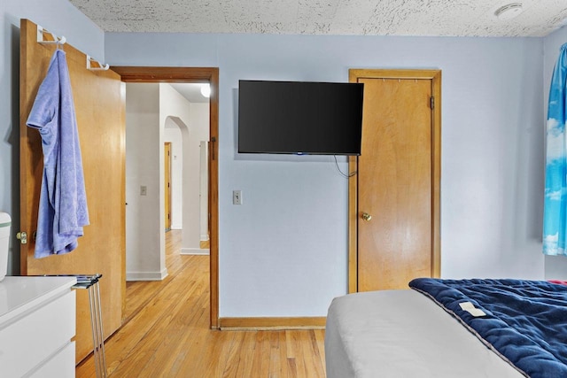 bedroom featuring arched walkways, light wood finished floors, and baseboards