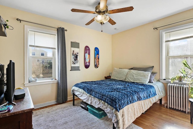 bedroom featuring baseboards, wood finished floors, a ceiling fan, and radiator