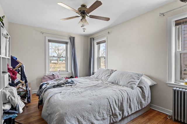 bedroom featuring baseboards, wood finished floors, a ceiling fan, and radiator