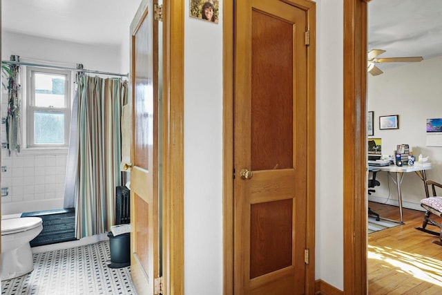 bathroom with shower / bath combination with curtain, toilet, a ceiling fan, wood finished floors, and baseboards