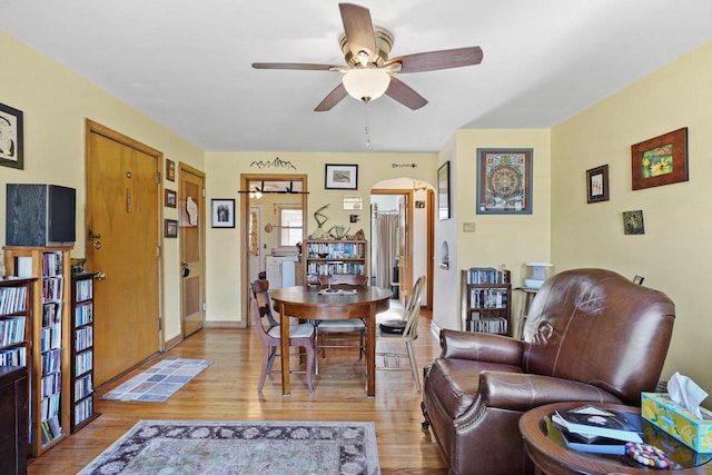 living room with light wood-style flooring, arched walkways, and a ceiling fan