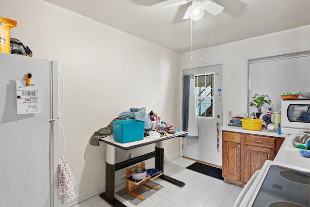 kitchen featuring brown cabinetry, a ceiling fan, stove, freestanding refrigerator, and light countertops