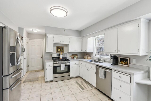 kitchen with light tile patterned floors, a sink, light countertops, appliances with stainless steel finishes, and white cabinetry