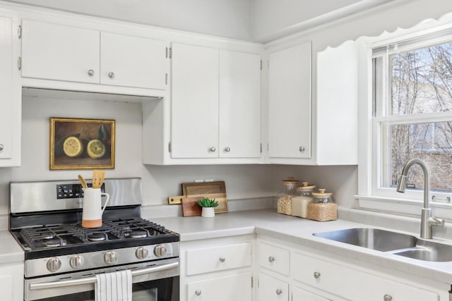 kitchen with stainless steel gas range oven, white cabinetry, light countertops, and a sink