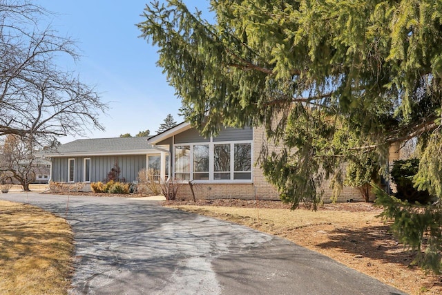 view of front facade with brick siding, board and batten siding, and driveway