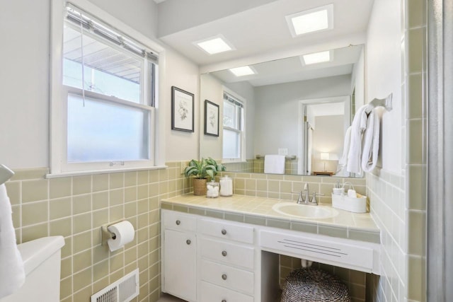 half bathroom featuring visible vents, toilet, tile walls, and vanity