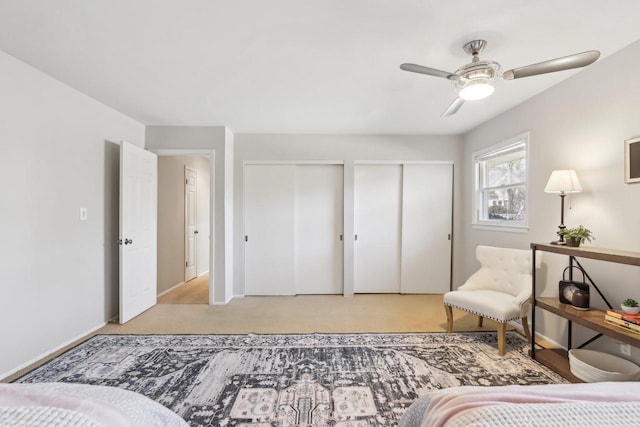 bedroom with light colored carpet, baseboards, two closets, and ceiling fan