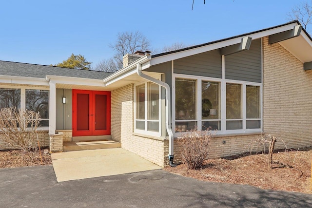 view of exterior entry with brick siding, a chimney, and a shingled roof