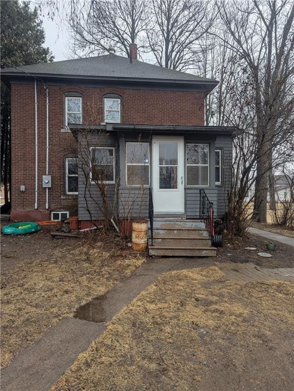 view of front facade featuring entry steps, brick siding, and a chimney