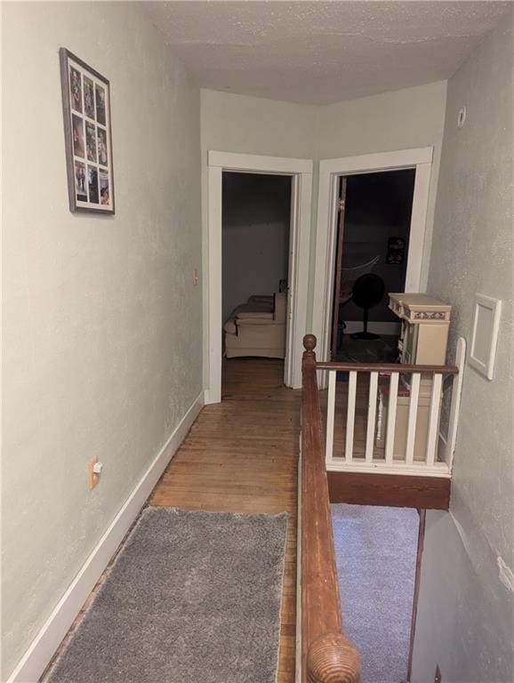 hall featuring a textured ceiling, baseboards, wood finished floors, and a textured wall