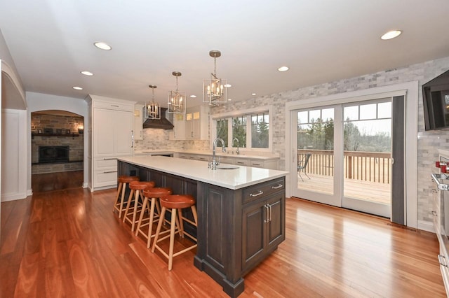 kitchen with light countertops, wall chimney range hood, wood finished floors, and a stone fireplace