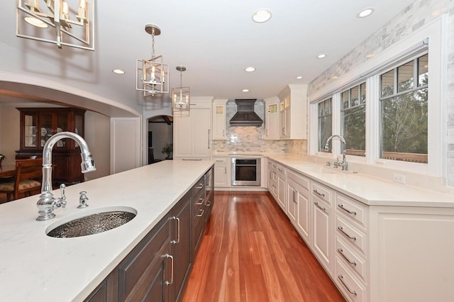 kitchen with premium range hood, white cabinetry, a sink, and oven