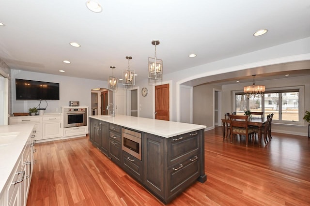 kitchen featuring arched walkways, stainless steel appliances, light countertops, light wood-style floors, and a sink