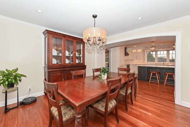 dining room featuring a chandelier, arched walkways, wood finished floors, baseboards, and crown molding