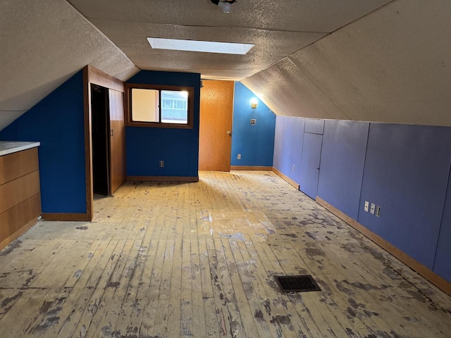 bonus room featuring a textured ceiling, vaulted ceiling with skylight, visible vents, and light wood-style flooring