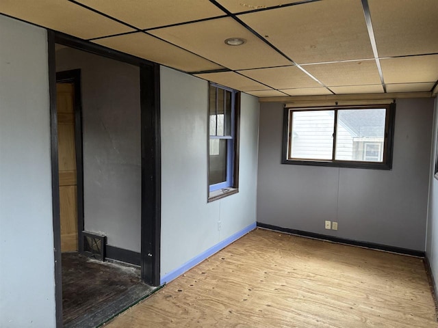 spare room featuring light wood finished floors, a paneled ceiling, and baseboards