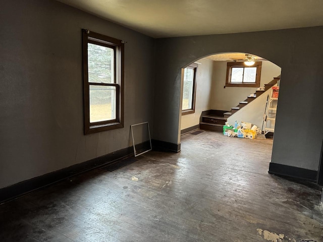 spare room featuring arched walkways, wood-type flooring, stairs, and baseboards