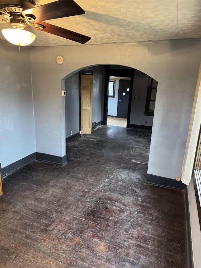 spare room with arched walkways, baseboards, and wood finished floors