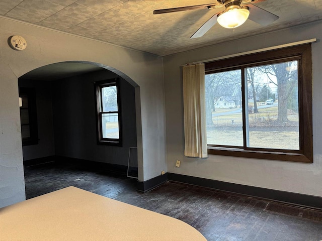 spare room with dark wood-style floors, arched walkways, visible vents, ceiling fan, and baseboards