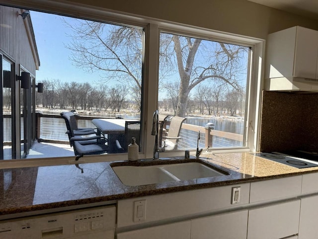 kitchen featuring dishwashing machine, electric stovetop, a sink, white cabinets, and dark stone countertops