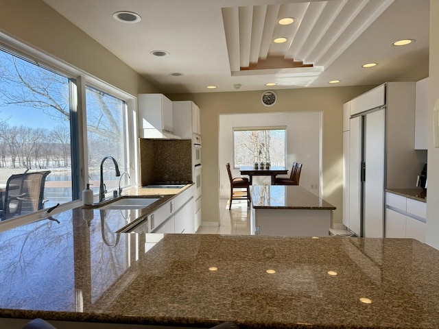 kitchen featuring a kitchen island, a sink, white cabinets, and a healthy amount of sunlight