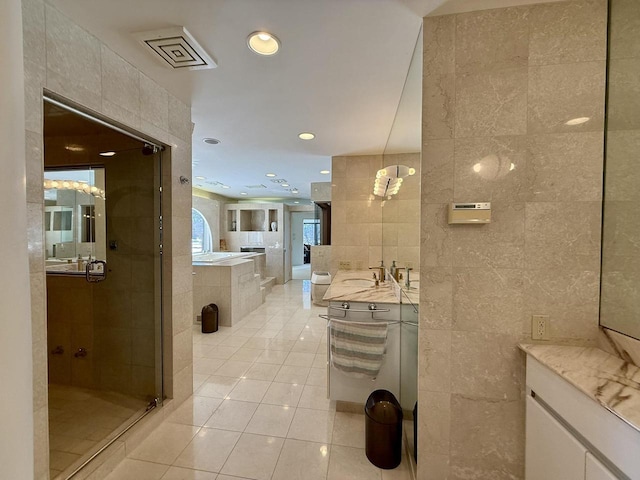 full bathroom with two vanities, tile walls, a shower stall, a bath, and tile patterned floors