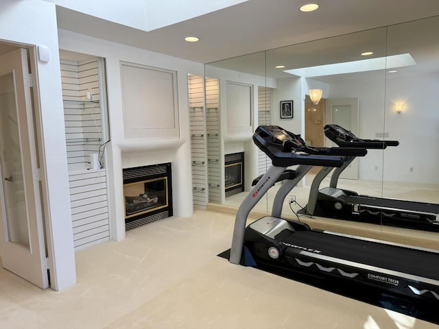 exercise room featuring carpet flooring, a glass covered fireplace, and recessed lighting