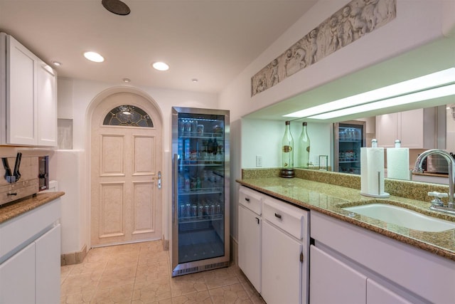 kitchen with light stone countertops, white cabinets, a sink, and refrigerator with glass door